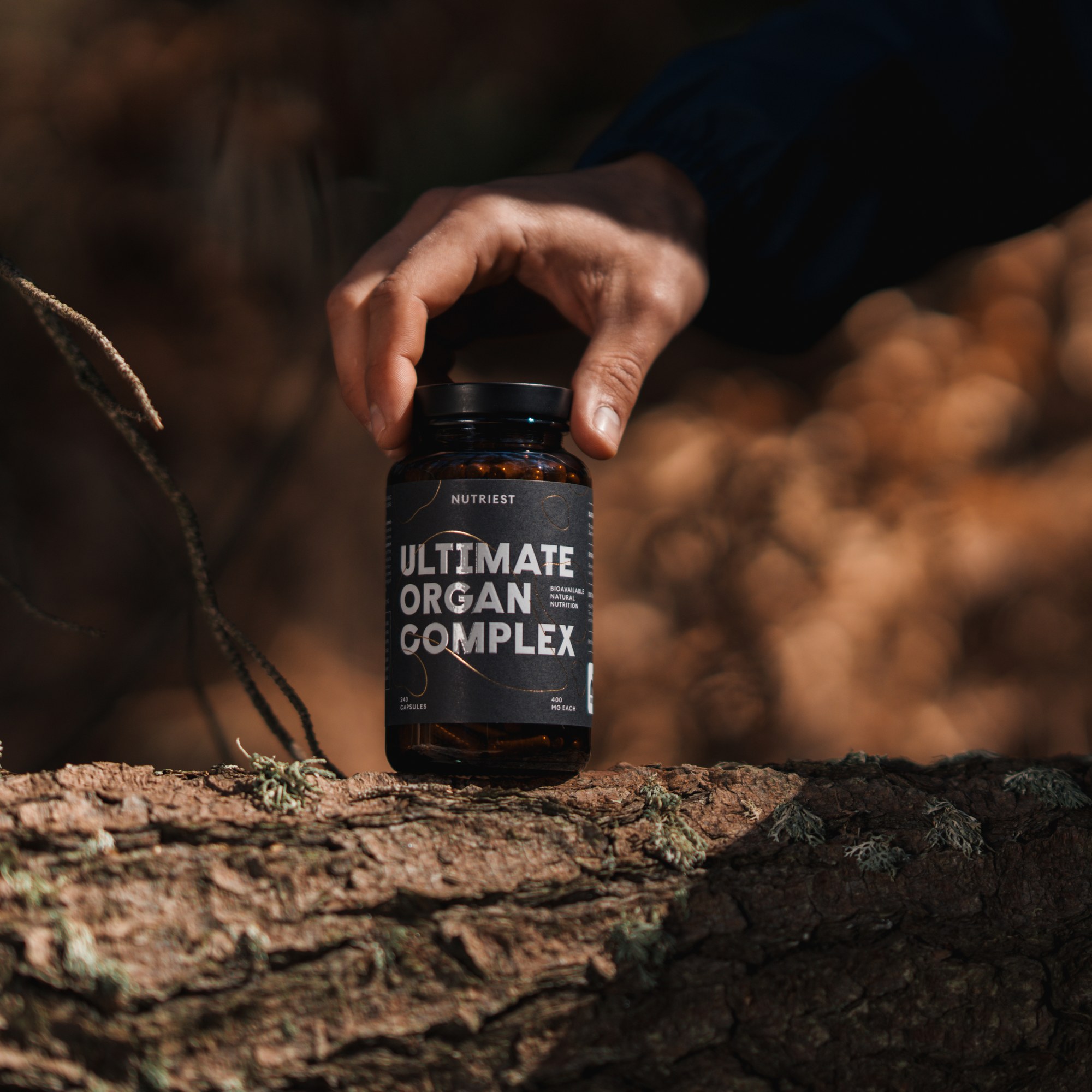 Hand placing Nutriest Ultimate Organ Complex on mossy log outdoors
